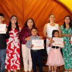 Niños y niñas con sus padres sonríen felices con sus reconocimientos en la ceremonia de premiación.