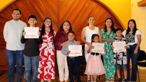 Niños y niñas con sus padres sonríen felices con sus reconocimientos en la ceremonia de premiación.